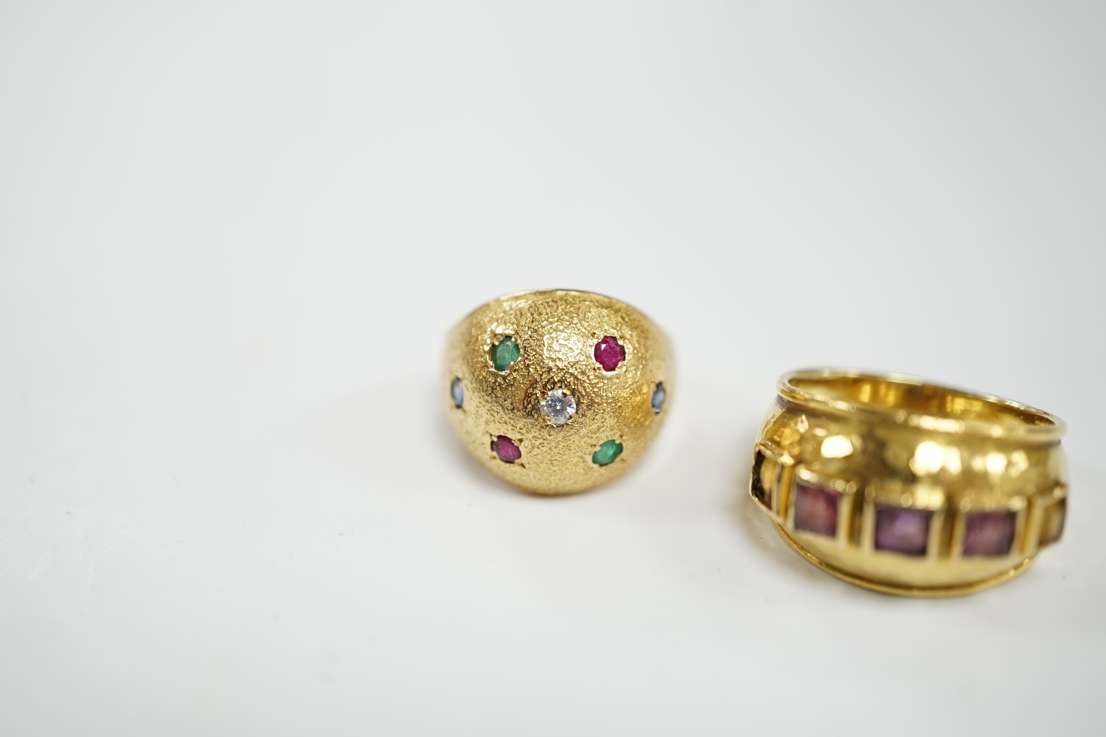A textured yellow metal, emerald, ruby and diamond set domed ring, size K, together with a stylish yellow metal and graduated square cut amethyst set five stone ring, size M, gross weight 13.1 grams.